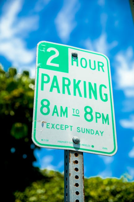 A blue parking sign with white symbols indicating accessible parking is mounted on a metal post in front of a dark grey textured wall. The sign displays a large white letter 'P' and a wheelchair symbol below it, designating designated disabled parking. The shadow of the sign is cast onto the wall, suggesting a light source from the left side of the image. The scene is outdoors, with no vehicles or other objects visible around the sign. This setting relates to parking regulations often encountered during house removals or furniture transport, and the sign’s placement indicates available accessible parking space likely relevant for relocating services by Man with Van Stanmore as part of their moving logistics. The image emphasizes the importance of planning around parking restrictions during home relocation tasks, especially in urban areas like Stanmore, where permits may be required from Harrow Council.